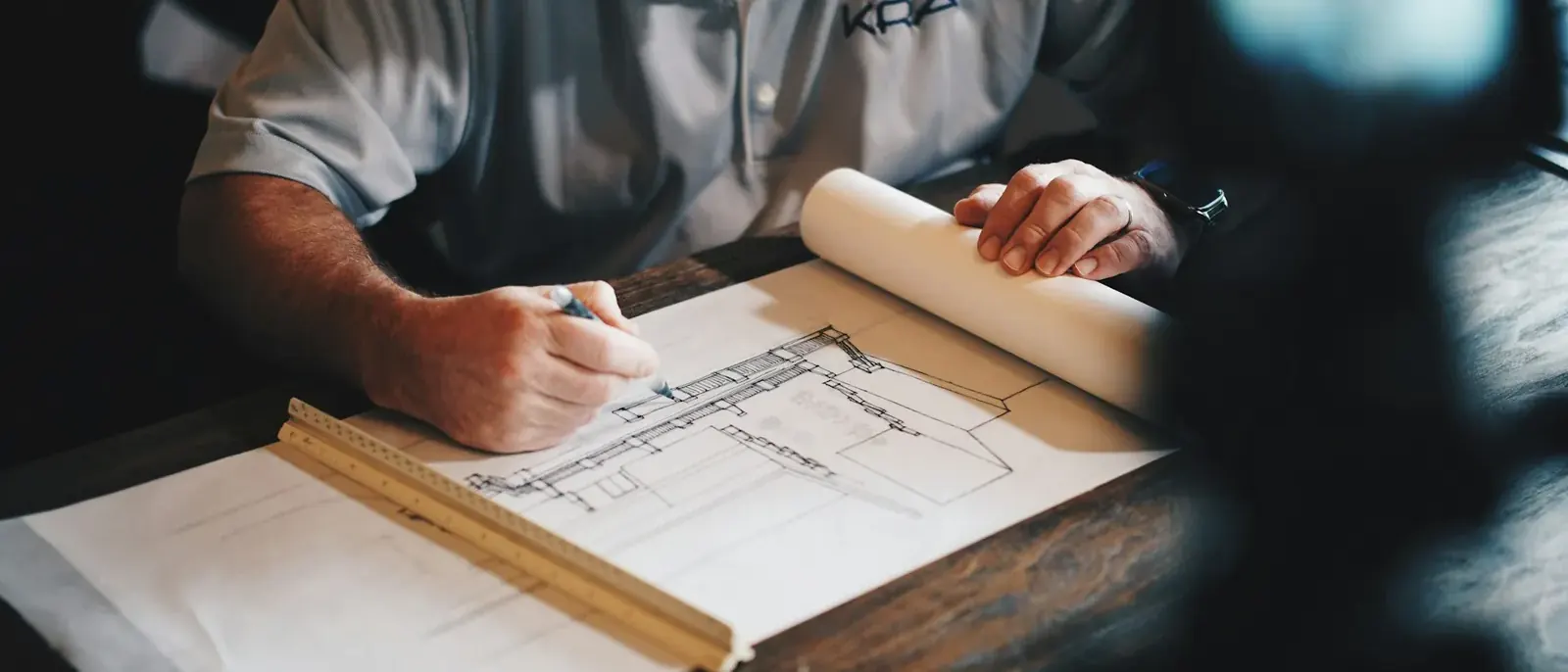 Mãos de arquiteto desenhando planta com lápis e régua, etapa de projeto que antecede o alvará de construção em Goiânia