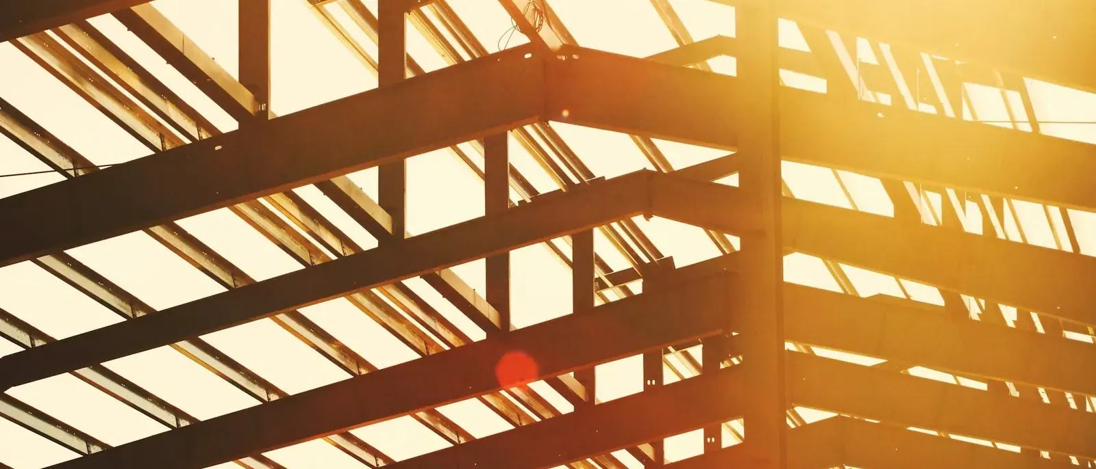 Estrutura metálica de cobertura vista de baixo contra o céu claro, com pilares, vigas e terças de aço, etapa de obra conduzida por construtora de galpão em Goiânia