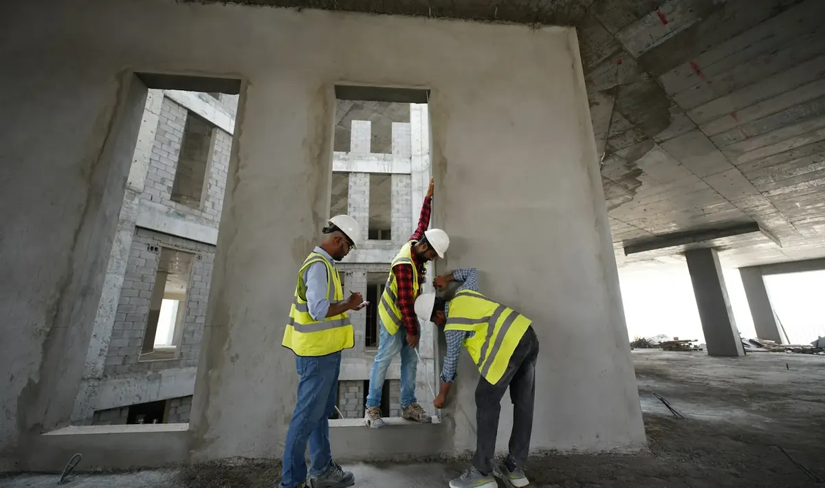 Três profissionais de capacete e colete medindo uma parede em prédio em obra, vistoria comum na consultoria de engenharia civil em Goiânia