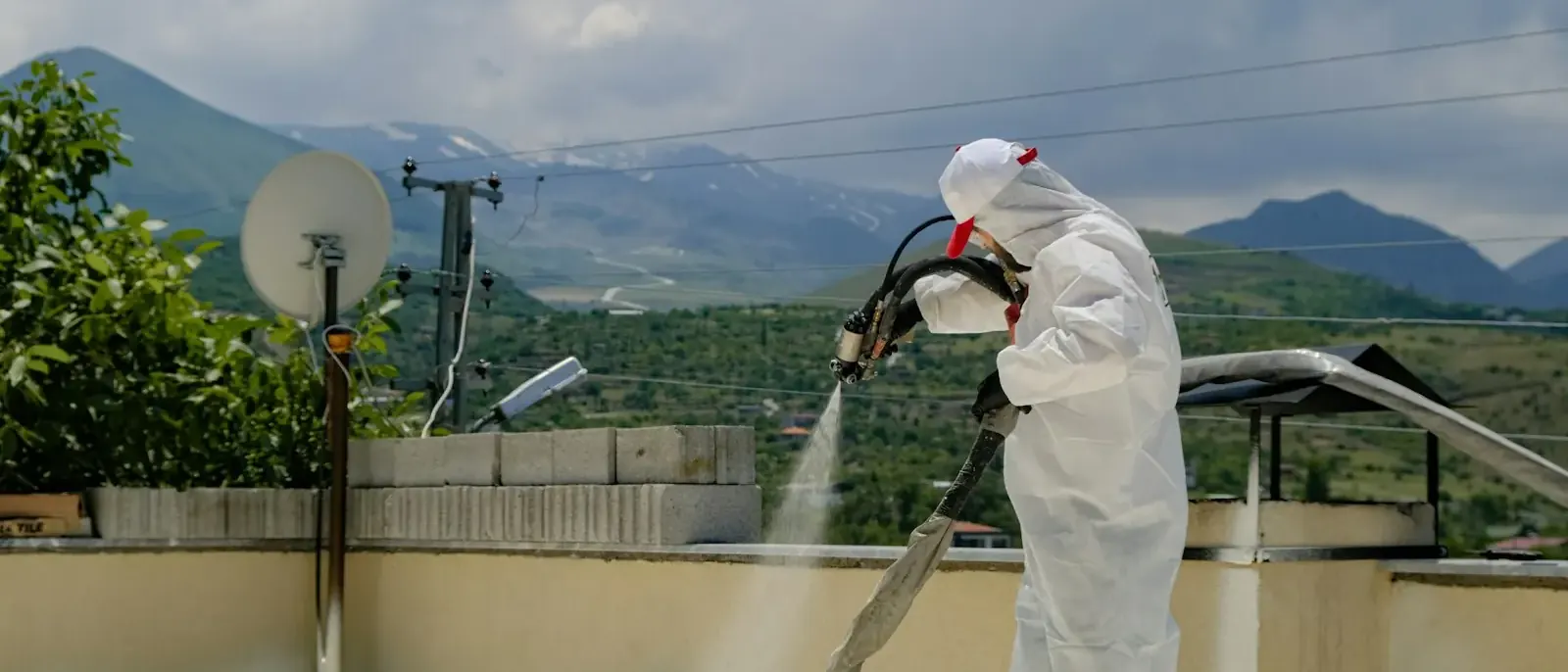 Aplicador de macacão branco pulverizando revestimento sobre a laje de uma cobertura, técnica usada na impermeabilização predial em Goiânia
