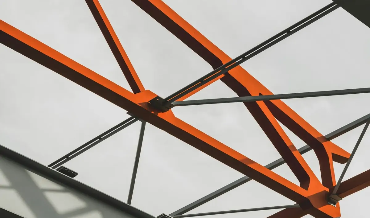 Vigas de aço com pintura laranja e tirantes metálicos contra o céu nublado, tipo de estrutura tratada na pintura industrial em Goiânia