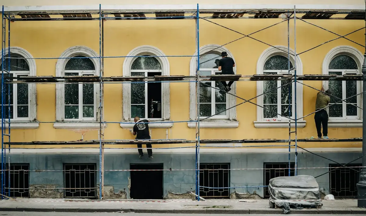 Três operários em andaime trabalhando na fachada amarela de um prédio com janelas em arco, serviço ligado à pintura predial em Goiânia
