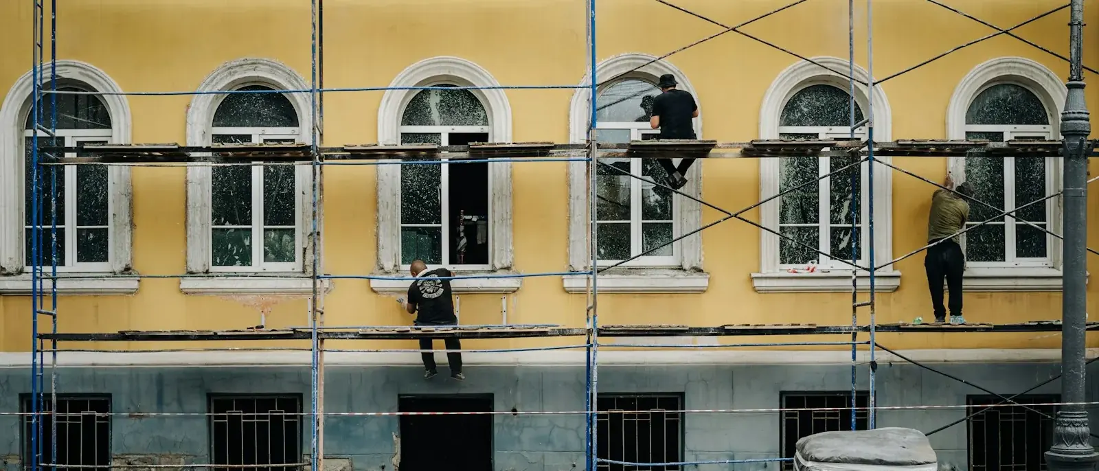 Três operários em andaime trabalhando na fachada amarela de um prédio com janelas em arco, serviço ligado à pintura predial em Goiânia