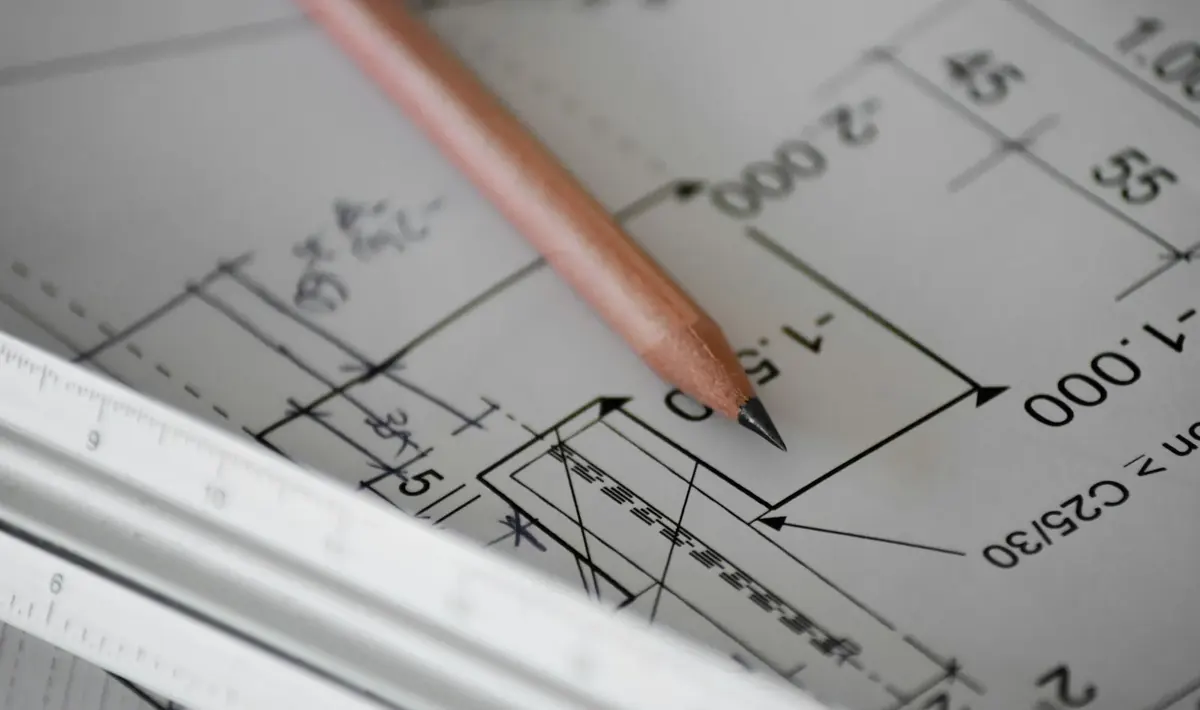 Lápis e escalímetro sobre prancha de desenho técnico com cotas e medidas, detalhe do trabalho de projetos de engenharia em Goiânia
