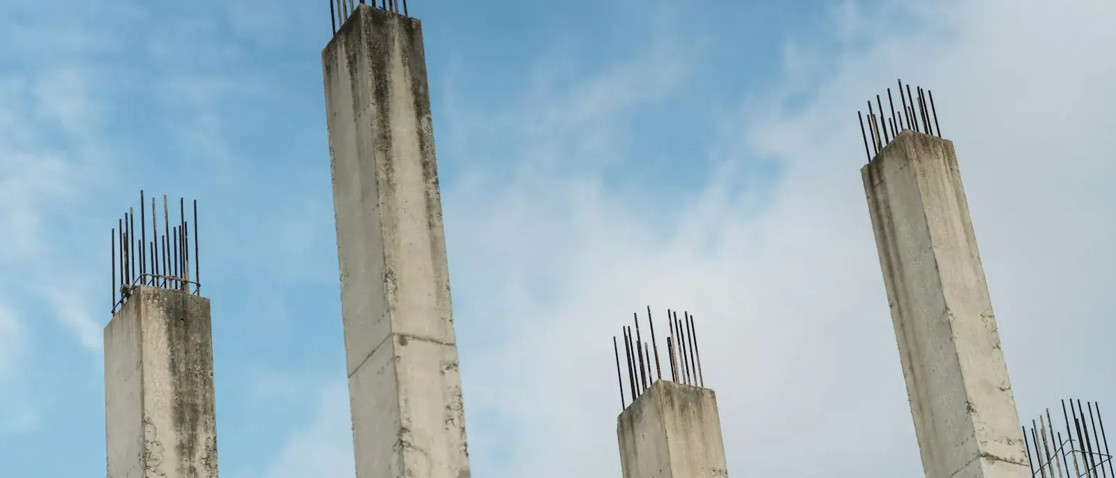 Pilares de concreto manchados pelo tempo, com barras de aço aparentes no topo, imagem que ilustra a recuperação estrutural em Goiânia