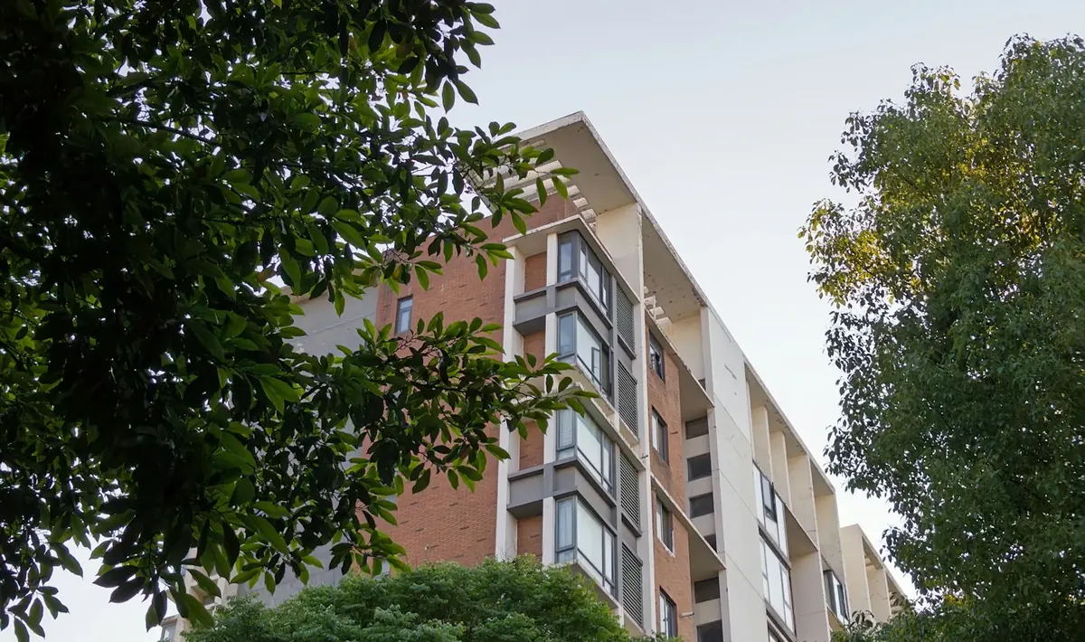 Prédio residencial de tijolo aparente e concreto visto entre árvores, tipo de edifício que passa por reforma de condomínio em Goiânia