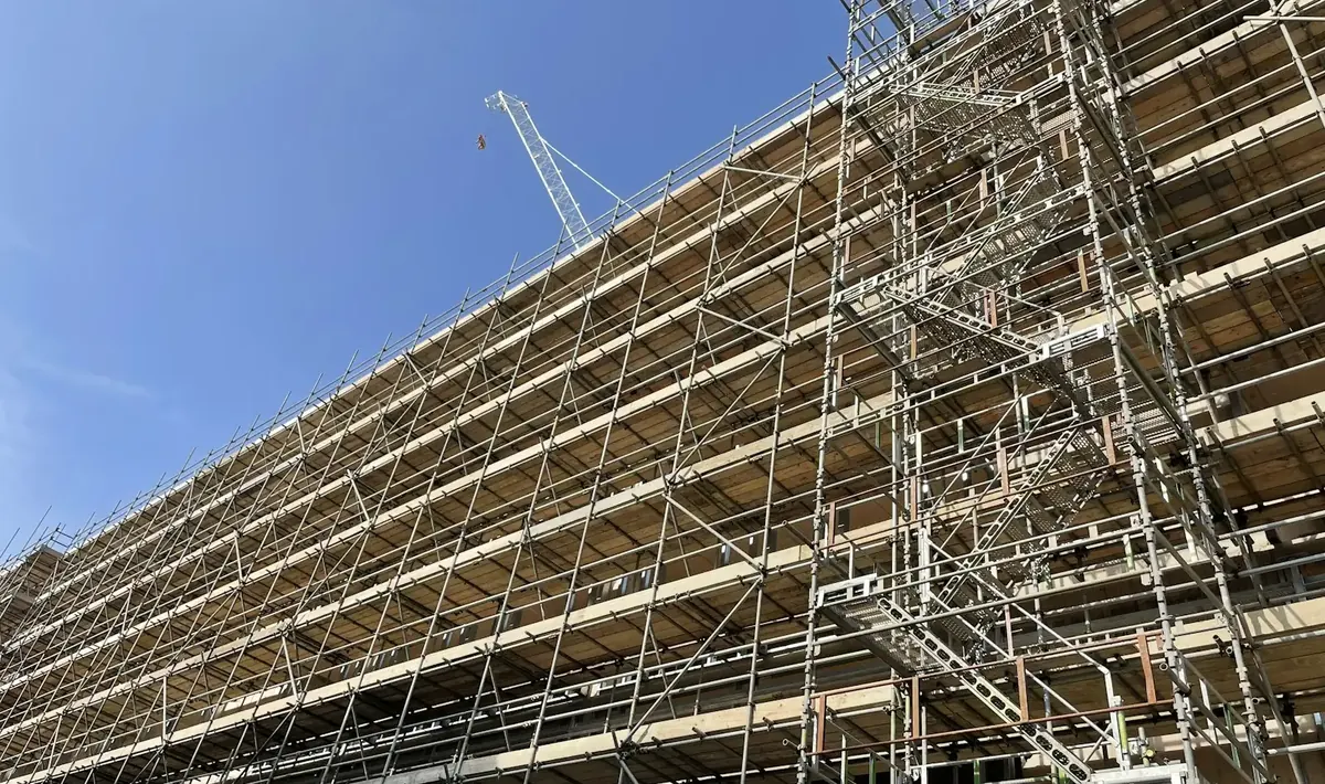 Edifício de vários andares coberto por andaimes tubulares, com grua ao fundo, etapa típica de uma reforma de fachada em Goiânia