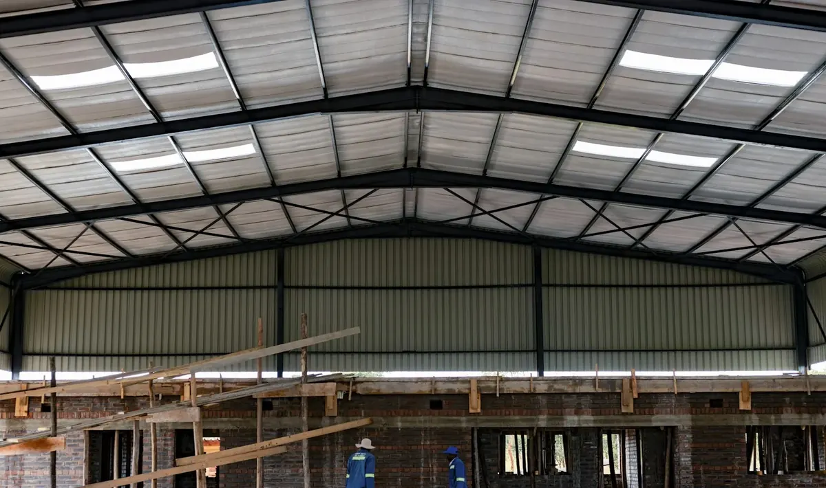 Interior de galpão com estrutura metálica, telhas com faixas translúcidas e fôrmas de madeira à frente, cenário de reforma de galpão em Goiânia