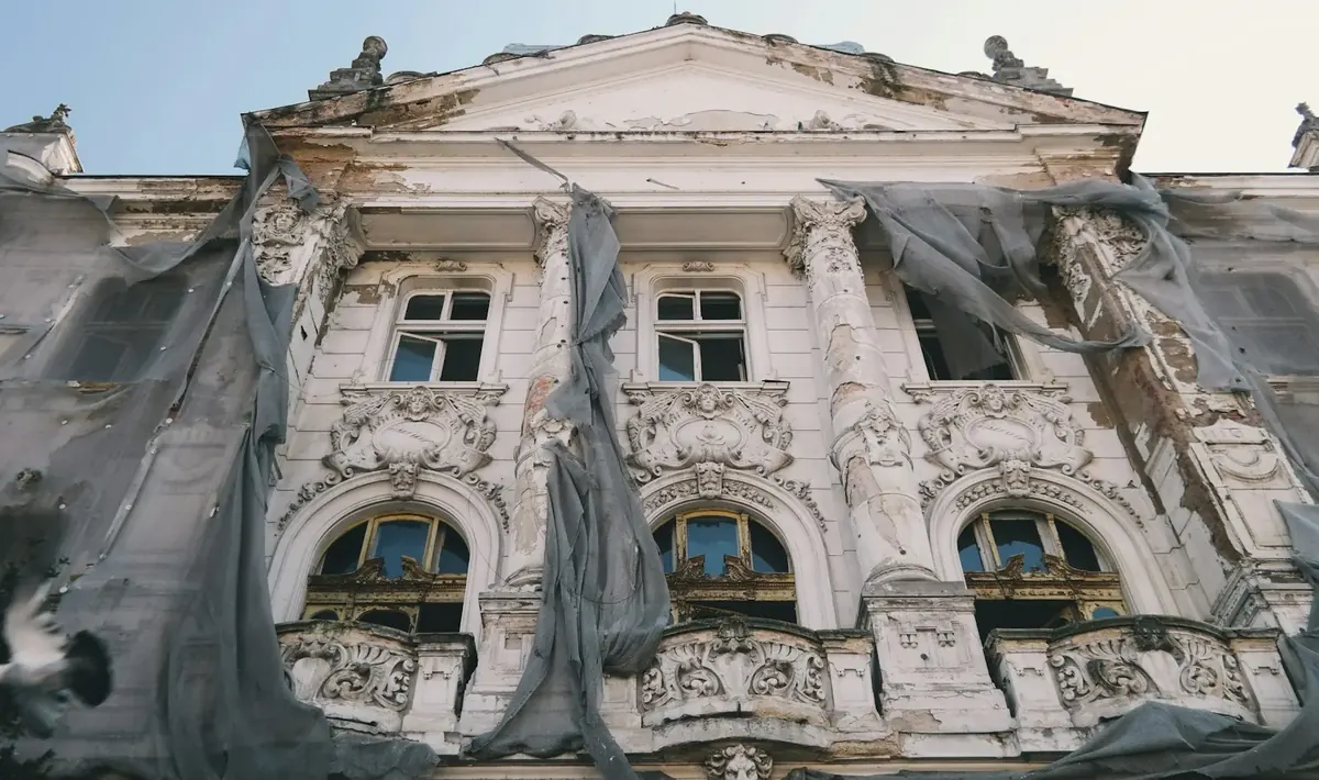 Fachada antiga ornamentada com pintura descascada e telas de proteção rasgadas, desgaste tratado no retrofit de edifícios em Goiânia