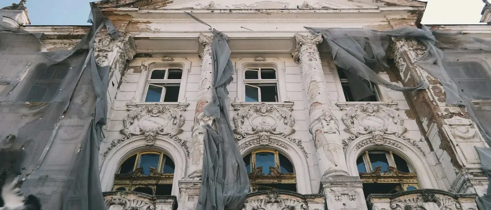 Fachada antiga ornamentada com pintura descascada e telas de proteção rasgadas, desgaste tratado no retrofit de edifícios em Goiânia